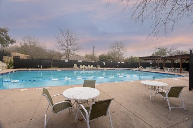 pool at dusk with a patio, a community pool, fence, and a pergola