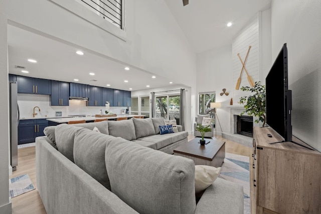 living area with recessed lighting, a large fireplace, light wood-style floors, and a towering ceiling