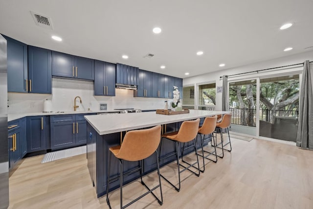 kitchen featuring visible vents, blue cabinetry, light wood-style flooring, a kitchen breakfast bar, and a center island