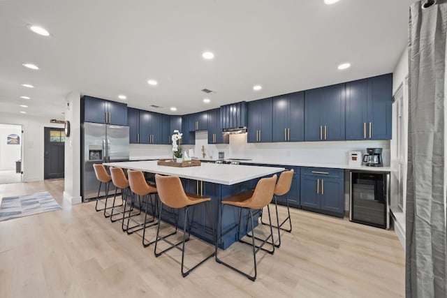 kitchen featuring beverage cooler, stainless steel fridge, light wood-type flooring, and blue cabinets