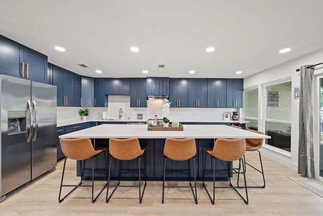 kitchen featuring visible vents, a large island, blue cabinetry, stainless steel fridge, and light countertops