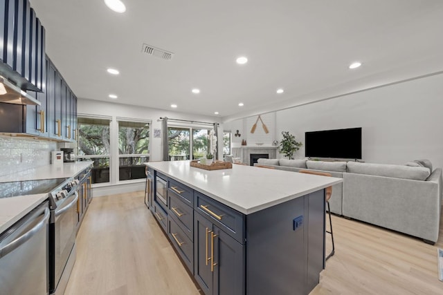 kitchen featuring visible vents, a kitchen island, light wood-style floors, appliances with stainless steel finishes, and decorative backsplash