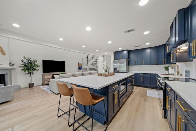 kitchen with light wood-type flooring, a kitchen bar, visible vents, open floor plan, and stainless steel appliances