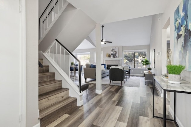 interior space with a fireplace, wood finished floors, a ceiling fan, and high vaulted ceiling