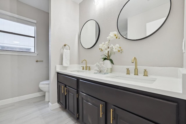 bathroom featuring double vanity, toilet, baseboards, and a sink