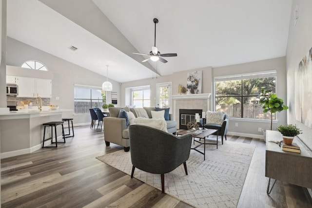 living area with light wood-type flooring, visible vents, a ceiling fan, baseboards, and a tile fireplace