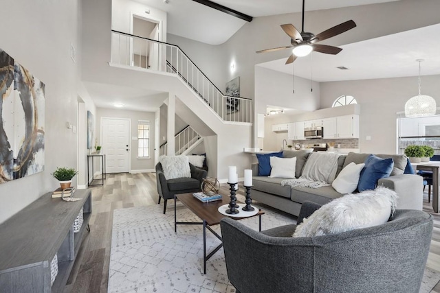 living room featuring baseboards, stairs, light wood-style floors, high vaulted ceiling, and a ceiling fan