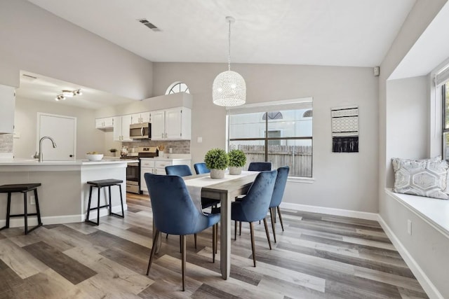 dining space with light wood-style floors, vaulted ceiling, baseboards, and visible vents