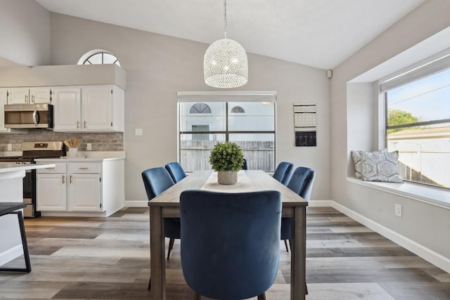 dining area featuring lofted ceiling, baseboards, and light wood finished floors