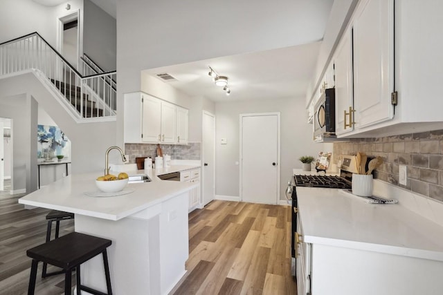 kitchen featuring light wood-type flooring, a sink, appliances with stainless steel finishes, a breakfast bar area, and a peninsula