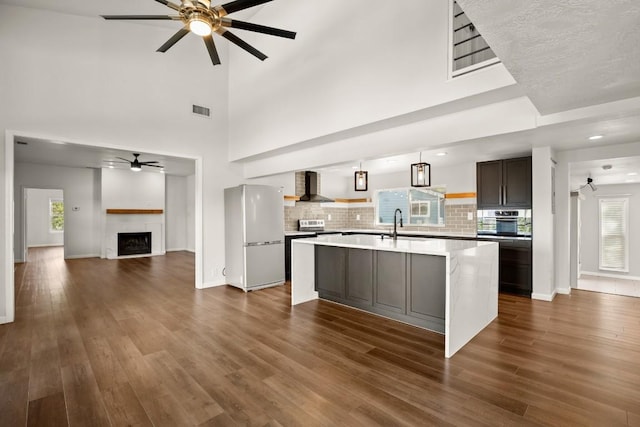 kitchen featuring wall chimney range hood, open floor plan, freestanding refrigerator, dark wood-style floors, and a ceiling fan