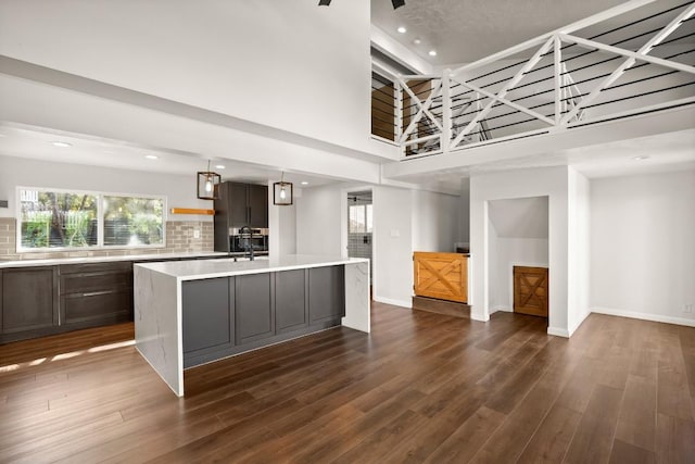 kitchen with an island with sink, backsplash, light countertops, and dark wood-style flooring