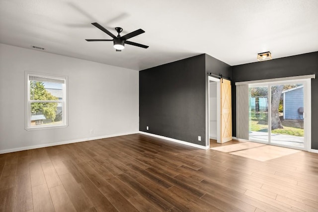 empty room featuring dark wood-style floors, baseboards, visible vents, ceiling fan, and a barn door