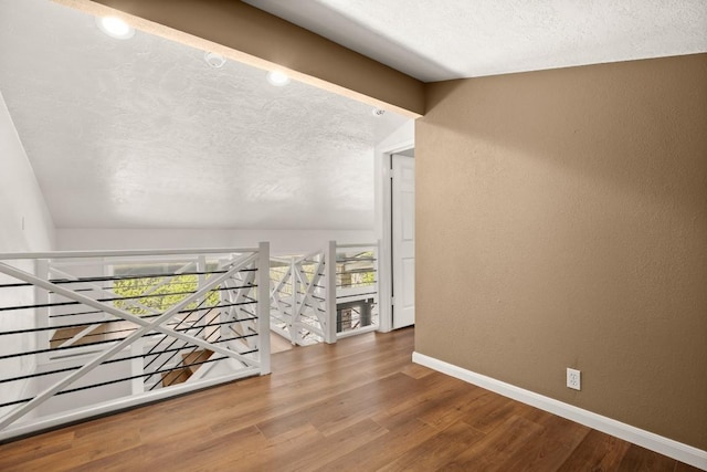 hall with an upstairs landing, a textured wall, baseboards, and wood finished floors