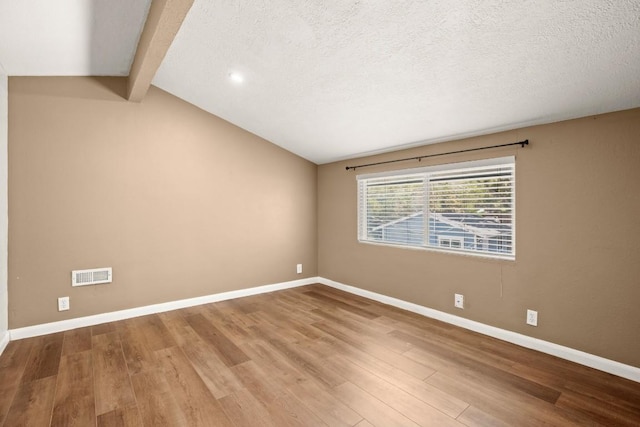 spare room featuring visible vents, a textured ceiling, baseboards, and wood finished floors