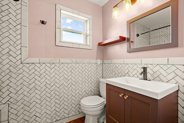 full bath featuring toilet, tile walls, wainscoting, walk in shower, and vanity