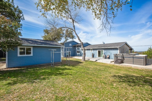 rear view of house with a lawn, a hot tub, and a patio
