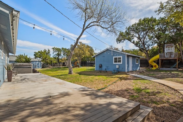 deck featuring an outbuilding, a lawn, a hot tub, and a playground