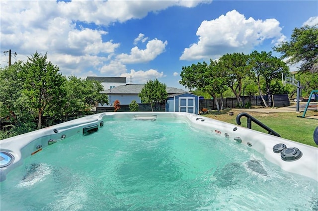 view of swimming pool with a storage unit, an outbuilding, fence, a yard, and a hot tub