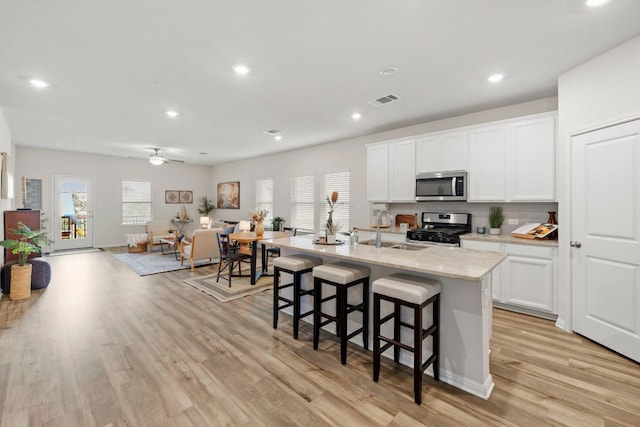 kitchen featuring visible vents, a sink, appliances with stainless steel finishes, a kitchen breakfast bar, and light wood-type flooring