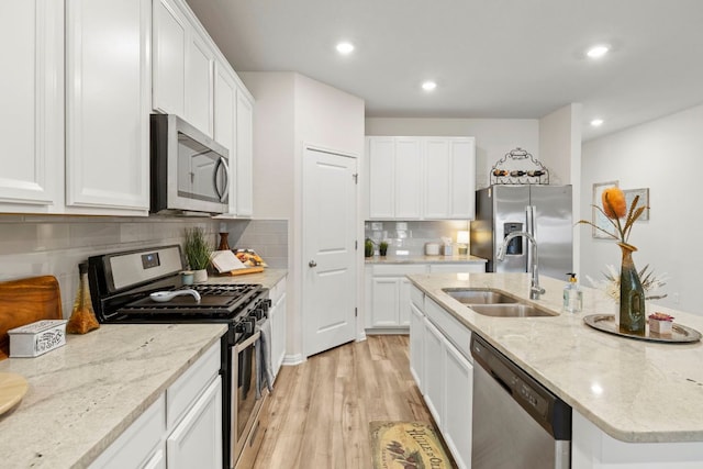 kitchen with an island with sink, a sink, white cabinetry, appliances with stainless steel finishes, and light wood finished floors