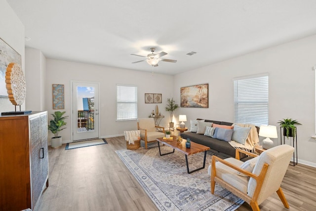 living area with visible vents, light wood-style flooring, baseboards, and ceiling fan