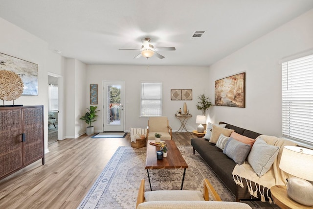 living room with light wood-style floors, a ceiling fan, visible vents, and baseboards