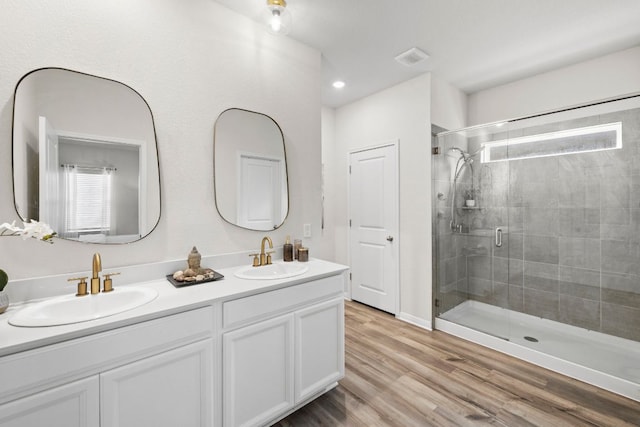 bathroom featuring double vanity, a stall shower, wood finished floors, and a sink