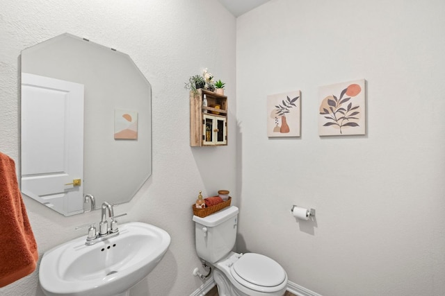 half bath featuring toilet, baseboards, and a sink