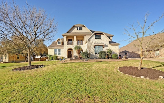 view of front of home featuring a front lawn, a balcony, and stone siding