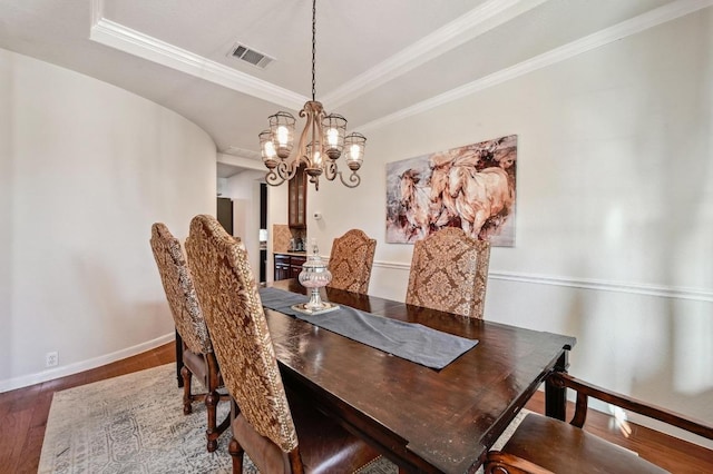 dining area with visible vents, a raised ceiling, an inviting chandelier, and wood finished floors