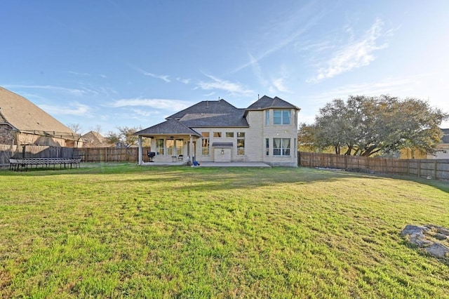 rear view of property featuring a patio area, a yard, a fenced backyard, and a trampoline