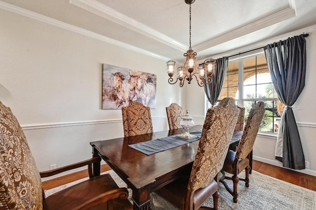 dining space with a notable chandelier, crown molding, a raised ceiling, and wood finished floors