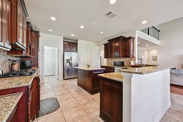 kitchen featuring light stone countertops, visible vents, a peninsula, stainless steel refrigerator with ice dispenser, and a center island