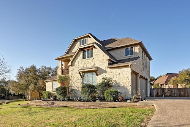 view of front of home with an attached garage, a front lawn, fence, stone siding, and driveway