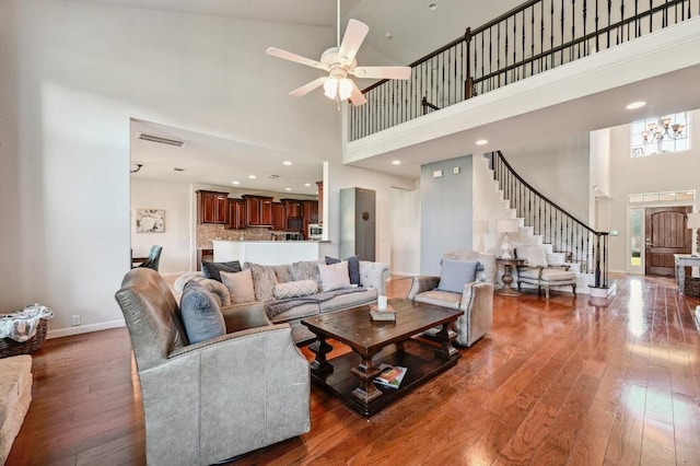 living area with visible vents, ceiling fan, baseboards, a towering ceiling, and hardwood / wood-style flooring