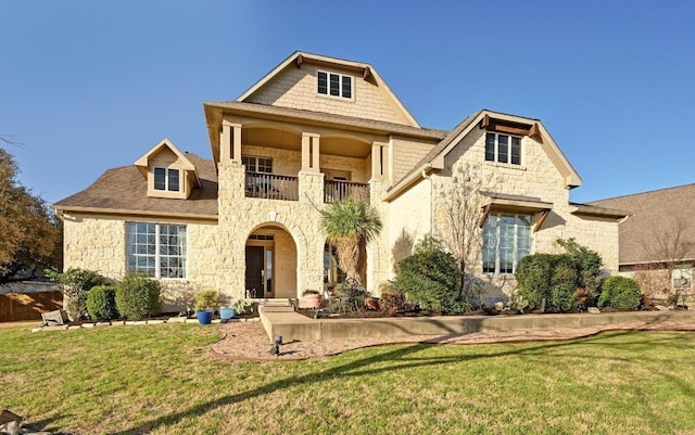 view of front facade with a front lawn, a balcony, and stone siding