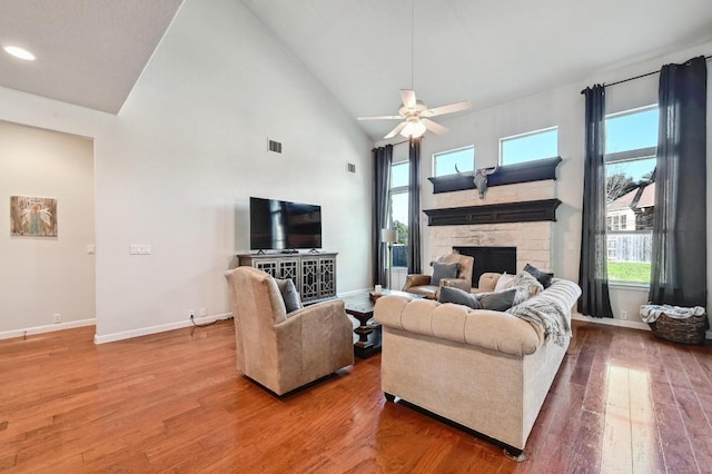 living room with visible vents, high vaulted ceiling, hardwood / wood-style floors, a stone fireplace, and ceiling fan