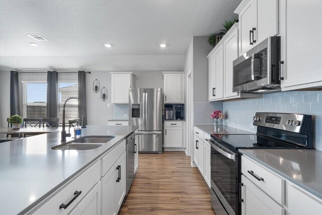 kitchen with visible vents, a sink, wood finished floors, appliances with stainless steel finishes, and white cabinets