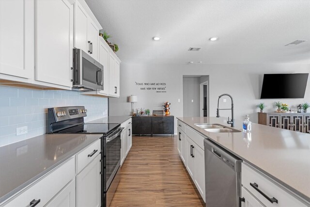 kitchen with wood finished floors, a sink, stainless steel appliances, white cabinets, and tasteful backsplash