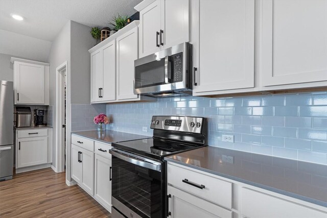 kitchen with light wood finished floors, decorative backsplash, appliances with stainless steel finishes, and white cabinetry