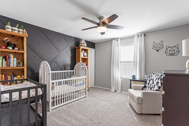 carpeted bedroom with baseboards, a crib, and a ceiling fan