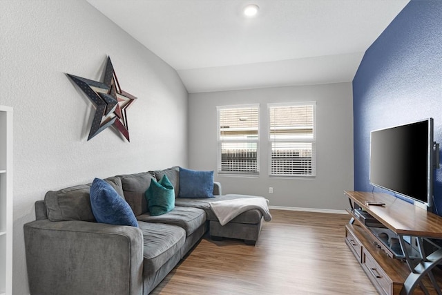 living area featuring vaulted ceiling, wood finished floors, baseboards, and a textured wall