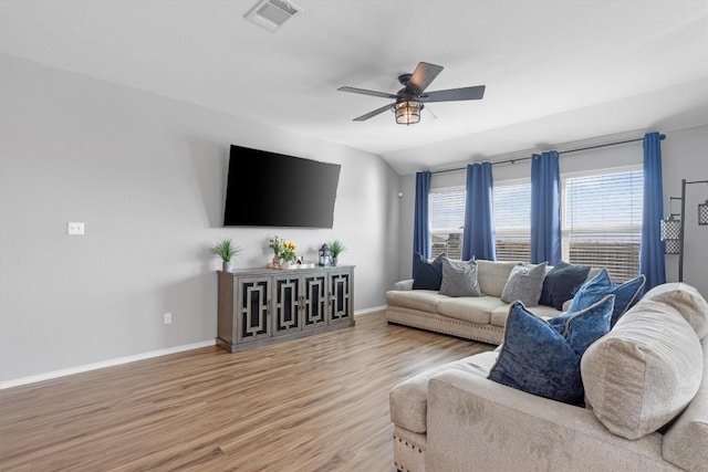 living area featuring visible vents, a ceiling fan, light wood finished floors, baseboards, and vaulted ceiling