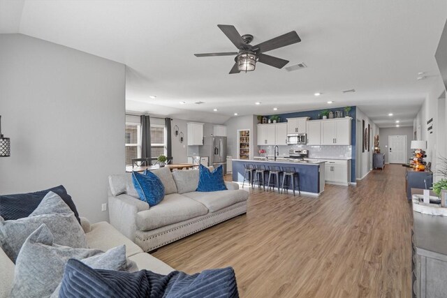 living area featuring a ceiling fan, visible vents, recessed lighting, vaulted ceiling, and light wood-style floors