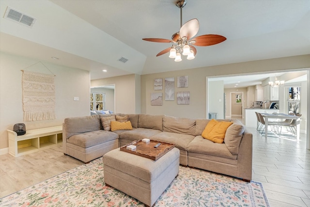 living area featuring visible vents, baseboards, lofted ceiling, light wood-style flooring, and ceiling fan with notable chandelier