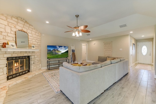 living area featuring a stone fireplace, visible vents, light wood finished floors, and ceiling fan