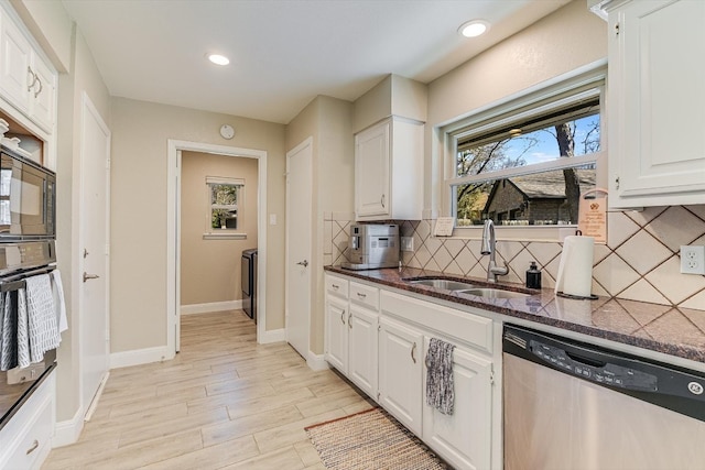 kitchen with oven, a sink, dark stone counters, white cabinets, and dishwasher