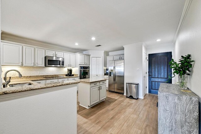 kitchen with a kitchen island, light wood-style flooring, a sink, appliances with stainless steel finishes, and crown molding