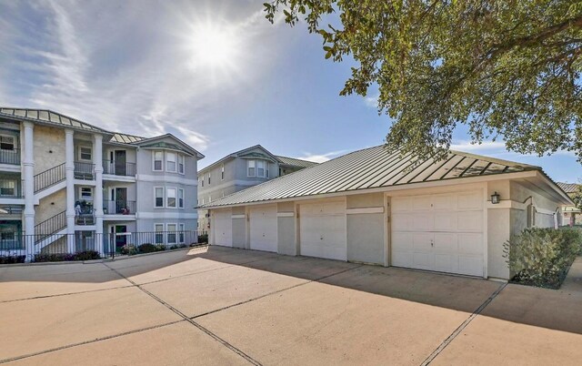 view of front facade with a standing seam roof, community garages, stucco siding, an outdoor structure, and metal roof